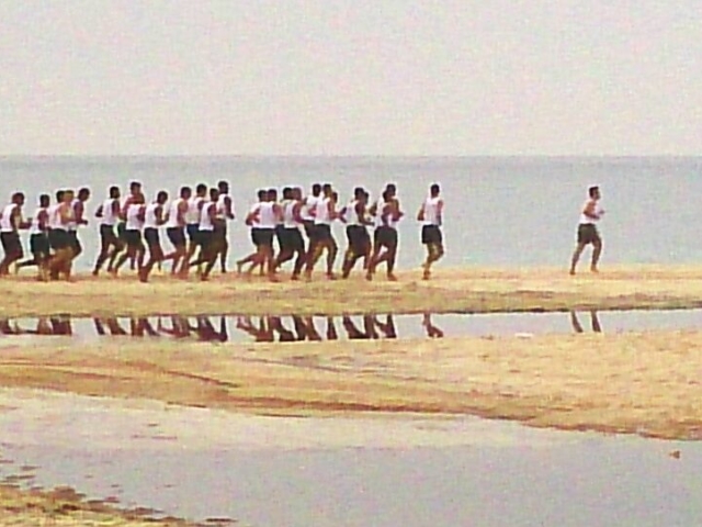 Grupa piłkarzy biegnących plażą
